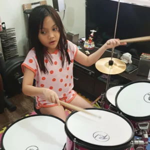 A young girl playing the drums at home, practicing coordination and rhythm skills.