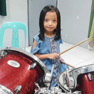 A young girl holding drumsticks at a drum set, ready to practice and build her musical skills.