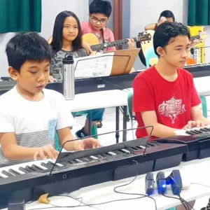 Students practicing keyboard and guitar together in a music class, focusing on group learning and performance.