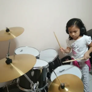 A young child playing the drums with headphones on, practicing rhythm and musical skills.